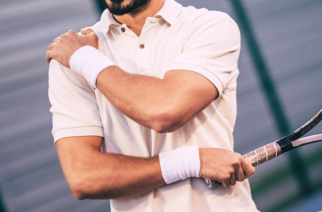 Un uomo vestito con una camicia con colletto tiene la spalla in una mano e una racchetta da tennis nell'altra.